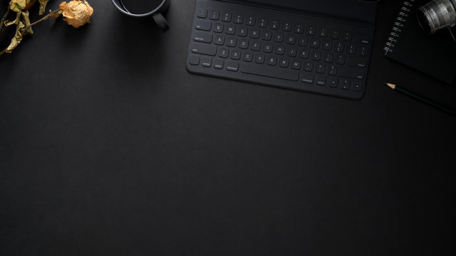 Top view of  workplace with wireless keyboard, copy space, camera and dry roses on black table