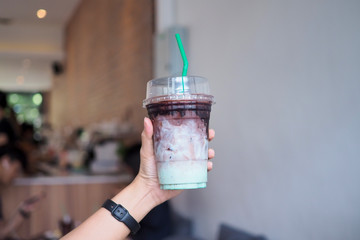 A plastic glass of iced black cocao with mint upper layer is cocao lower is pastel mint while middle is layer of fresh milk. selective focus.