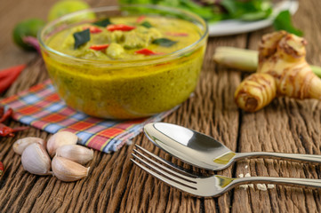 Green curry in a bowl with fork and spoon on wooden table.