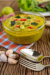 Green curry in a bowl with fork and spoon on wooden table.