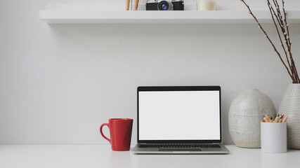 Cropped shot of workplace with blank screen laptop, red coffee cup, decorations on white desk