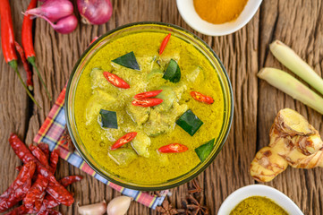 Green curry in a bowl and spices on wooden table.