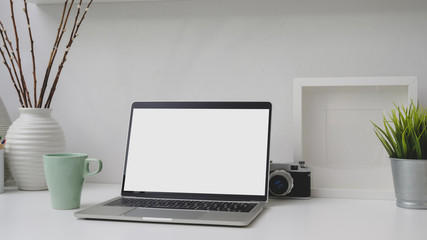 Cropped shot of workplace with blank screen laptop, frame, decorations and camera on white desk