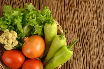 Bell pepper, tomato, onion, salad, and cauliflower on a wooden basket and wood table.