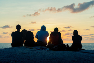 A group of young guys and girls meets dawn on a rock by the sea 