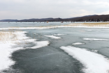 Melting snow with ice on the Big Lake with fishermen in the distance in the spring. Krasnoyarsk region. Russia.