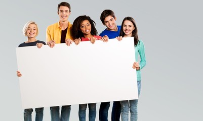 Group of diverse multiethnic happy young people posing with a blank white rectangular sign