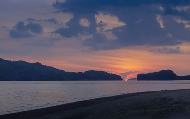 view seaside evening on long beach of limestone mountain in the sea with orange sun light and cloudy sky background, sunset at Pak Bara Beach, La-ngu District, Satun, southern Thailand.