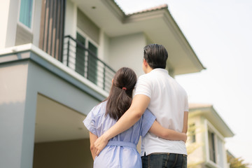 Back portrait of Asian young couple standing and hugging together looking happy in front of their new house to start new life. Family, age, home, real estate and people concept..