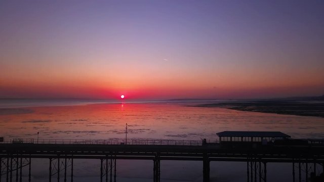 flying sideward parallel aerial shot with drone tracking Southend on sea essex pier train returning to depot with deep red orange sunset in background