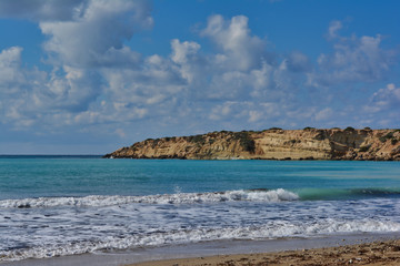 a sea Bay with azure sea water and a rocky cliff in the distance against a colorful cloudy sky