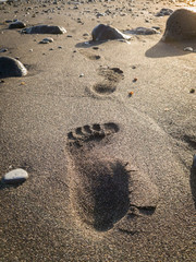 Closeup image of male footrpint on the black sand on the beach at sunset