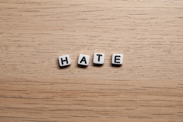 Word HATE in white cubes on light wooden background for your design templates