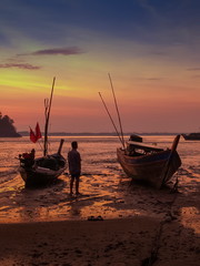 view seaside morning silhouette fishing boats and a fisherman on the beach with red sun light and blue sky background, sunrise at Mu Ko Phetra National Park, Satun, Thailand.