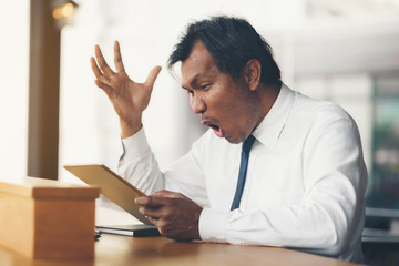 A middle-aged businessman holding a tablet is shocked by what happened to the screen.