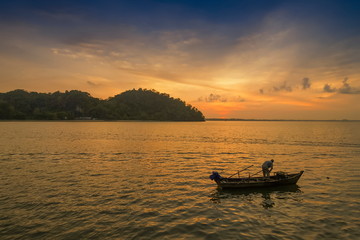 view seaside morning of a fisherman working in fishing boat floating in the sea with yellow sun light and blue sky background, sunrise at Mu Ko Phetra National Park, Satun, Thailand.