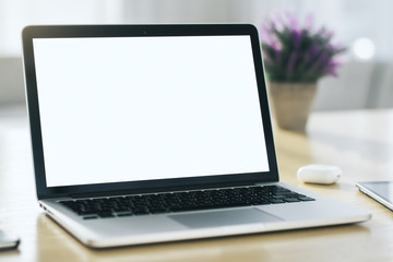 Fototapeta premium Close up of modern laptop with blank screen on table in sunny interior, mockup. Business and technology concept