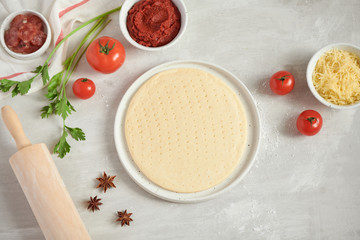 Fresh dough pizza base and ingredients on a white table. Top view.