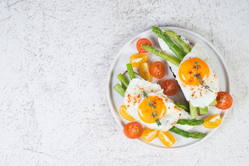 Crispy toast with cream cheese cream, fried egg and asparagus in a plate on a white background.
