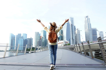 Young woman traveler with backpack and hat traveling into Singapore city downtown. Travelling in...