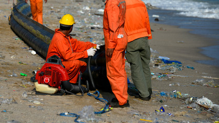 Worker setup equipment for clean spill oil at  beach and blurred foreground of plastic bottles...