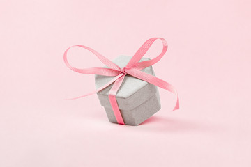 Gift box of irregular shape tied with a pink ribbon on a pink background. Festive minimalism concept. Copy space.