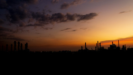 Oil refinery or chemical plant silhouette with night lights on at sunset.