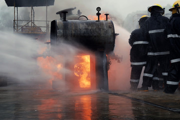 Fireman training Spray water curtain ,The Back side view of a group of firefighters helped stop the fire. Fire in the Industrial Factory . Rescue ,Education ,Emergency and Teamwork concept .