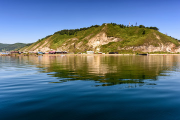 ake Baikal close to village Port Baikal, Russia. Horizontal day view of the high shore, green forest, houses, clear lake water