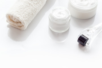 Obraz na płótnie Canvas Dermaroller for home cosmetologic procedure near creams on white background copy space