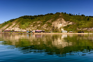 ake Baikal close to village Port Baikal, Russia. Horizontal day view of the high shore, green forest, houses, clear lake water