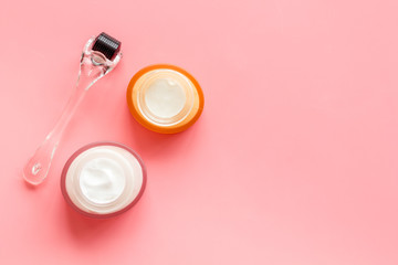 Dermaroller for mesotherapy near creams on pink background top-down copy space