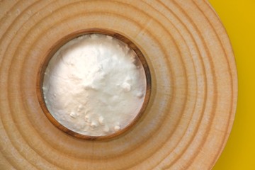 Baking soda. Sodium bicarbonate  in a wooden round cup on a wooden  dish on a yellow background.