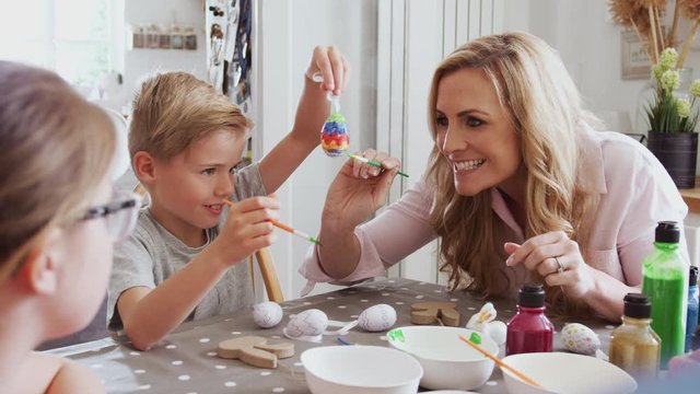 Parents With Children Sitting At Table Decorating Eggs For Easter At Home