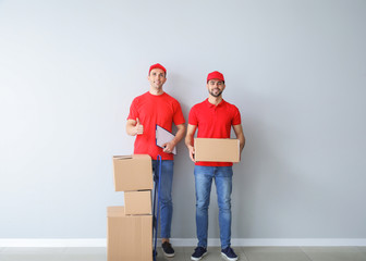 Delivery men with boxes near light wall