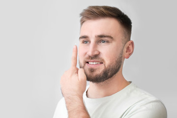 Young man putting in contact lenses on grey background