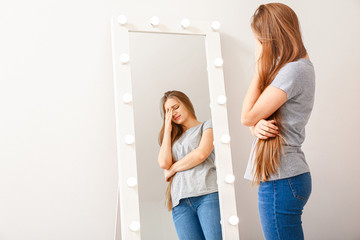 Displeased young woman near mirror at home - obrazy, fototapety, plakaty