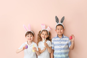 Little children with Easter eggs and bunny ears on color background