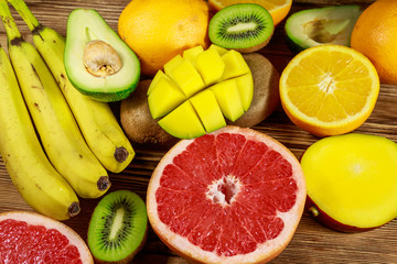 Assortment of tropical fruits on wooden table. Still life with bananas, mango, oranges, avocado, grapefruit and kiwi fruits