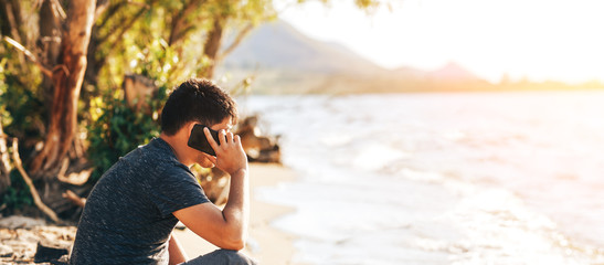 Young man looking at news and messaging and talking on his smart phone at beach and seaside. Hello...