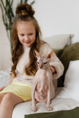 Obraz premium little pretty happy girl in home clothes playing, caring and cuddling with a cat, pet in a cozy children's bedroom, love friendship care family