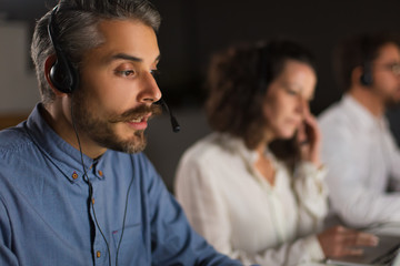 Handsome young man with headset looking at laptop screen. Confident bearded call center operator at...