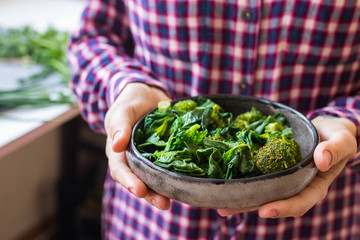 Green cooked broccoli, spinach salad meal. Hands hold bowl or plate. Vegan healthy diet food.