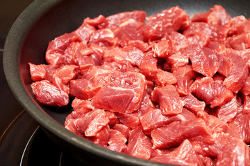Frying pan with raw pork chopped into small pieces for cooking goulash. Kitchenware. Background texture