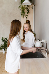 Happy mother and daughter in home white shirts relax in a hammock, have Breakfast and drink tea in the kitchen, have fun, communicate, hug in a cozy bright house, comfort, love, care, family, nature