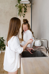 Happy mother and daughter in home white shirts relax in a hammock, have Breakfast and drink tea in the kitchen, have fun, communicate, hug in a cozy bright house, comfort, love, care, family, nature