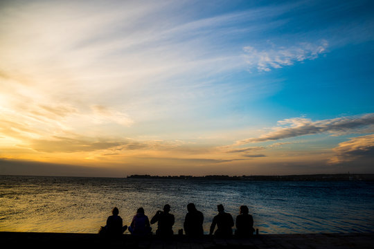 Silhouette of friends hanging out by the sea at sunset
