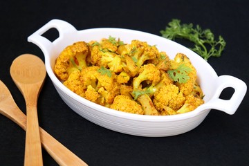 Dry cauliflower curry or Gobhi ki sabji or Gobi Masala served in white bowl with wooden spoons and coriander over white background with copy space.