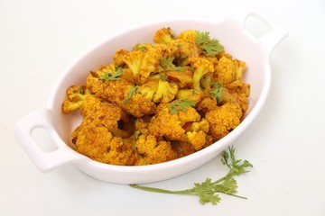 Dry cauliflower curry or Gobhi ki sabji or Gobi Masala served in white bowl with wooden spoons and coriander over white background with copy space.