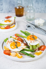 Crispy toast with cream cheese cream, fried egg and asparagus in a plate on a white background.
